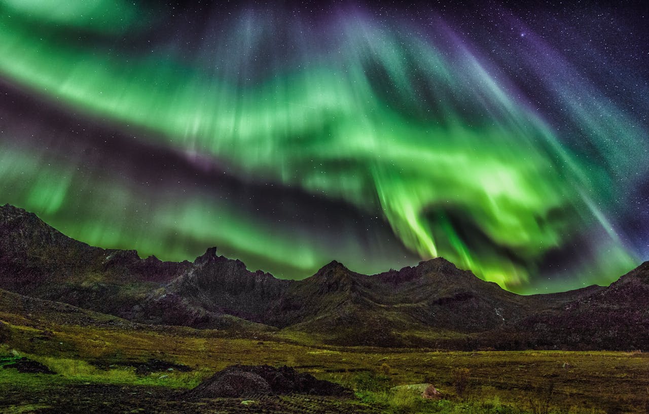 Stunning green Aurora Borealis lighting up the night sky over mountains, offering a breathtaking natural spectacle.